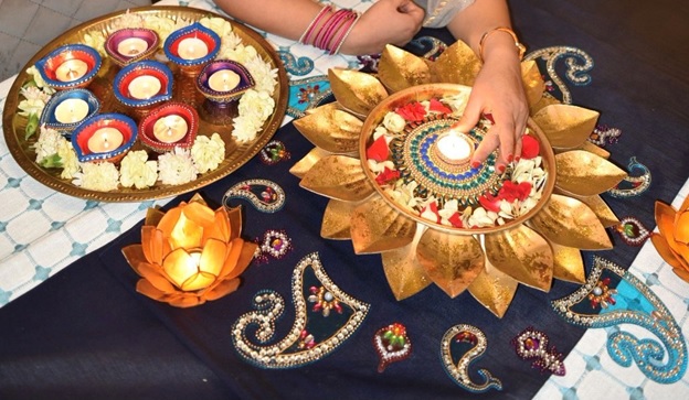 2 gold platters with flower petals surrounding lit candles in the center