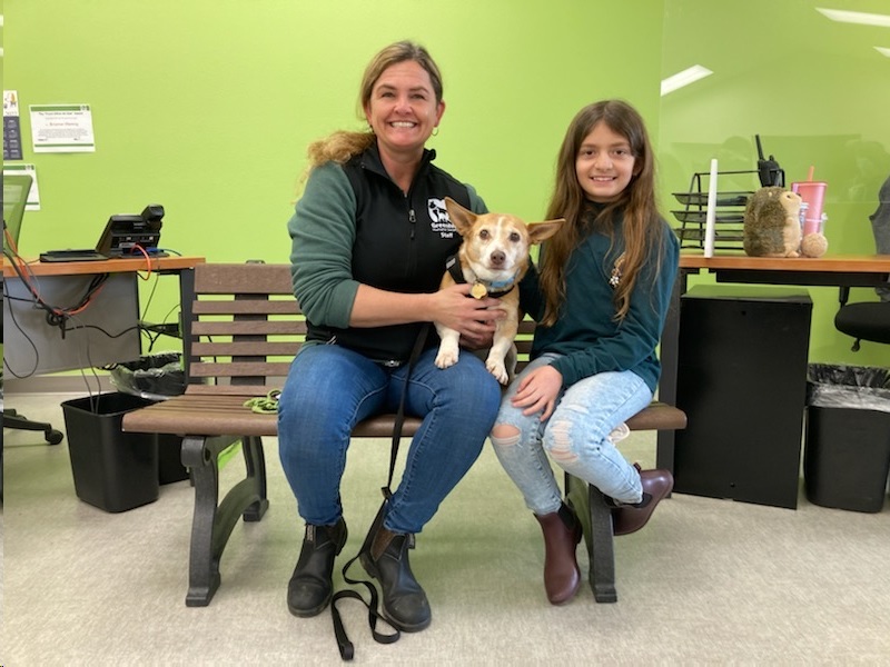 Megan and Emerie sit on a bench with a dog at Greenhill Humane Society