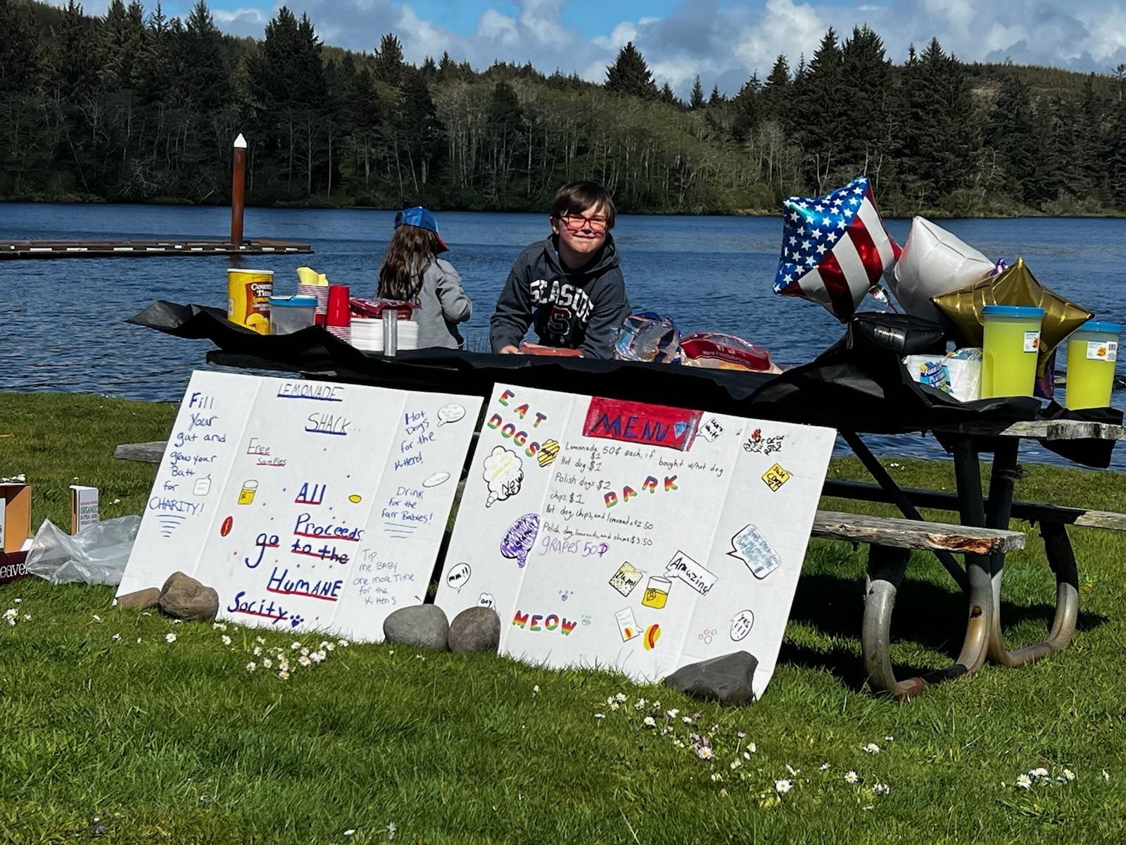 Two kids at a lemonade stand by the lake