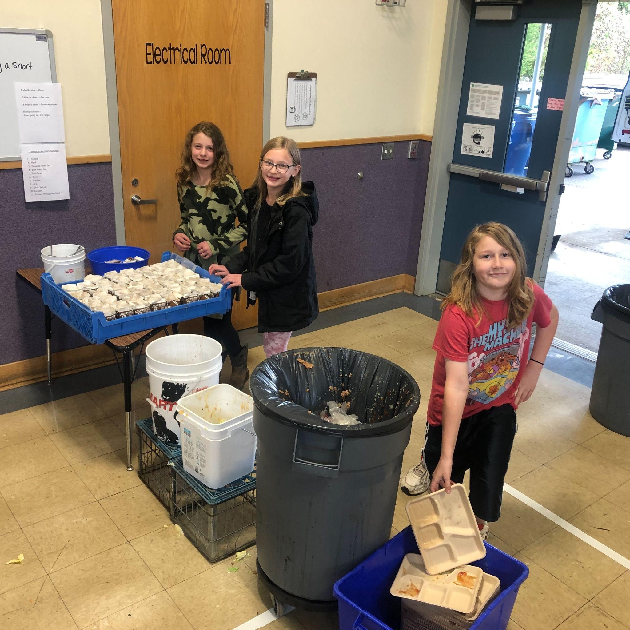 Three kids are composting cardboard and food scraps in bins at school
